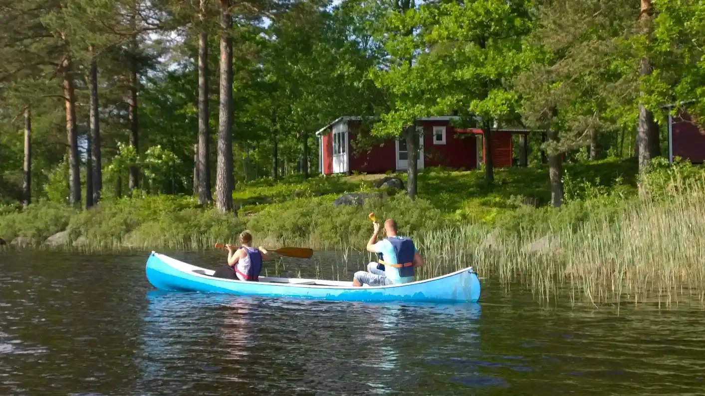 En roddbåt ligger vid strandkanten på Långasjönäs camping & stugby, omgiven av en lugn vattenyta och frodig natur, idealisk för utomhusaktiviteter och rekreation.