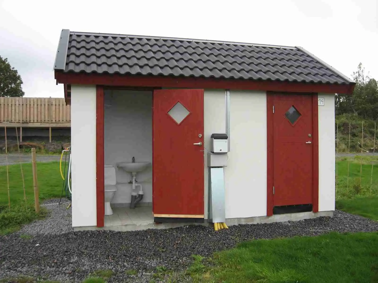 En liten trädgårdsbod med en dörr av kompositmaterial, omgiven av lummiga gröna växter vid Stråvalla camping.