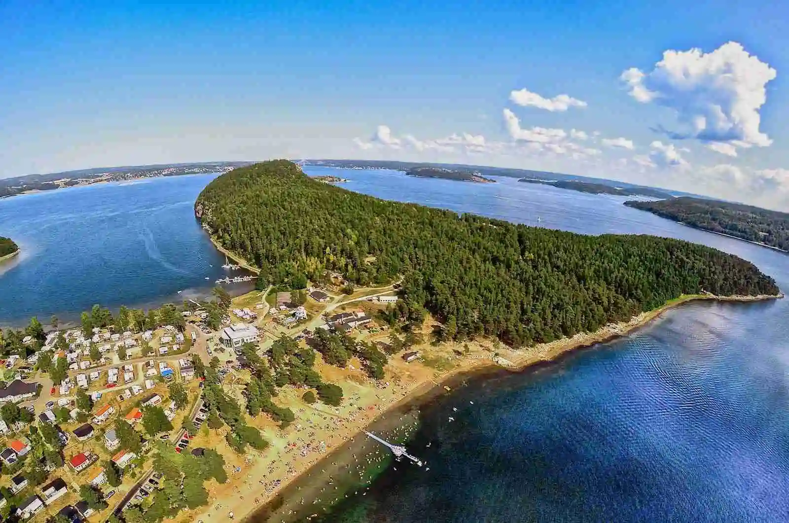 Flygbild över Hafsten Resort & Camping, med en vy av en kustlinje som möter ett lugnt hav. Stranden omges av bukter och vikar, vilket ger en inbjudande och naturskön miljö.