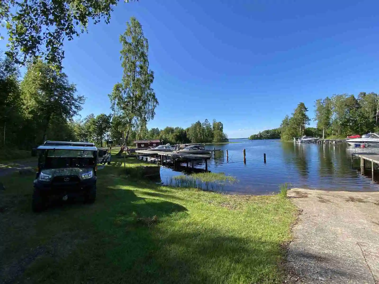 En vy över en stillsam flod eller kanal vid Löckna camping, med flera båtar förtöjda längs med stranden och omgivande grönska.