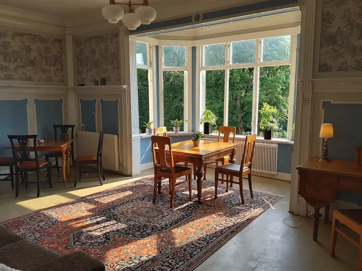 Ett interiörfoto av Hunnebergs Gård Hostel & Camping som visar ett träinrett rum med bord och stolar, parkettgolv och enkel takbelysning.