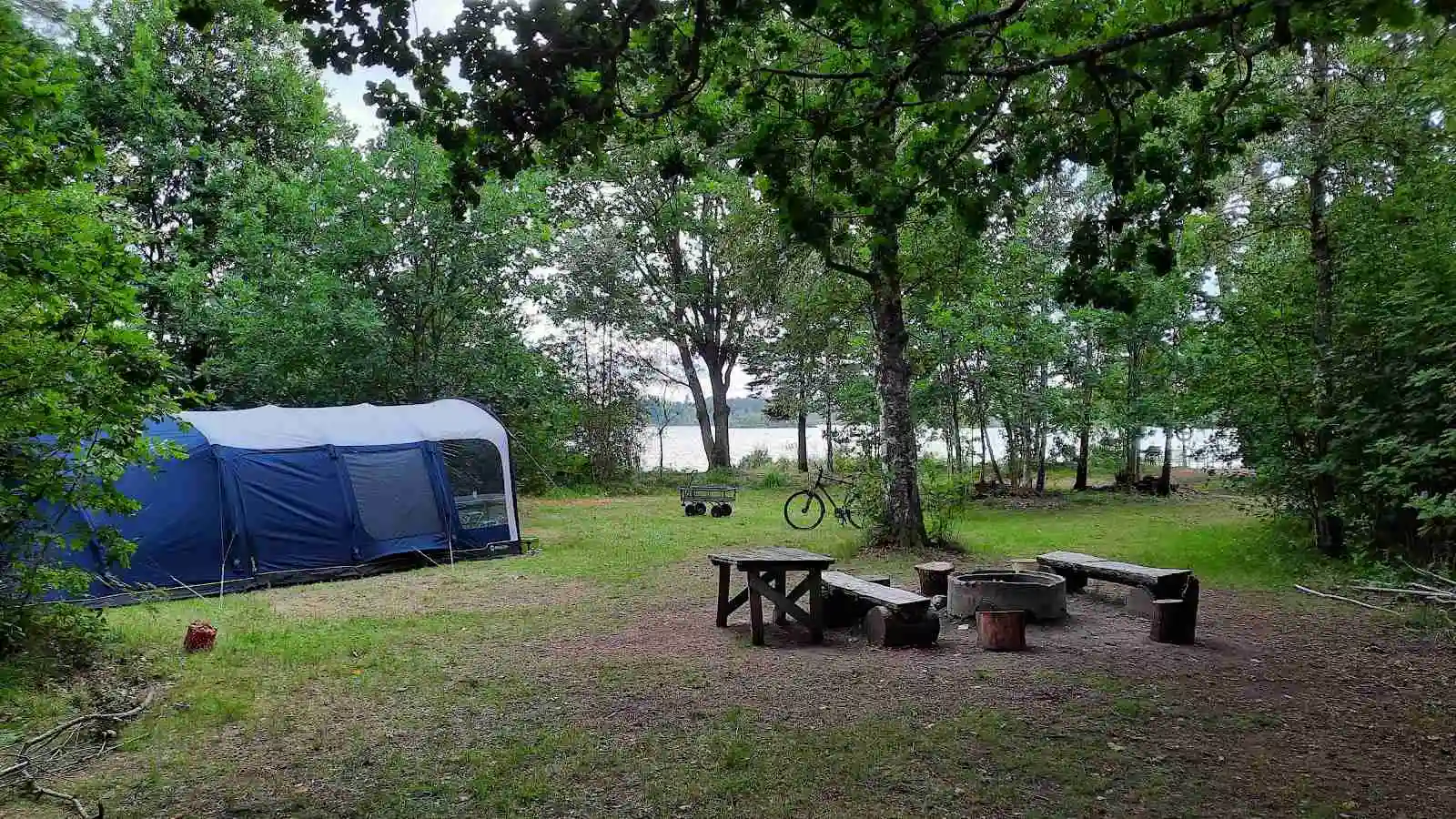 En campingplats vid Agundaborg Camp & Paddle med tält, skuggande presenning, picknickbord och bänkar i en grönskande parkmiljö.