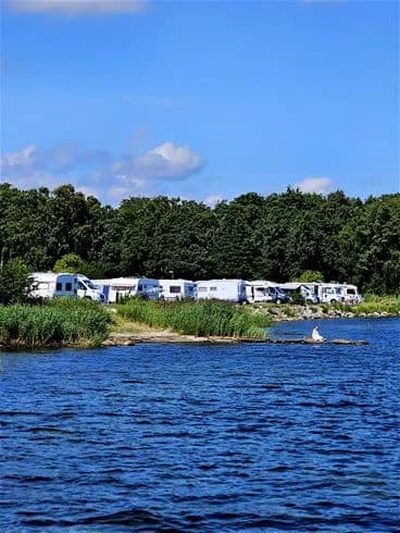En lugn vattenväg omgiven av grönskande träd och en sandstrand, perfekt för sommaraktiviteter vid My Camping Tredenborg.