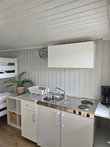 Ett modernt campingkök med trägolv och stilren inredning. Köket är utrustat med vitvaror, inklusive en spis och kylskåp, samt ljusa träbänkar och skåp. Atmosfären är inbjudande och funktionell, vilket gör det till en bekväm plats för matlagning under campingvistelsen.