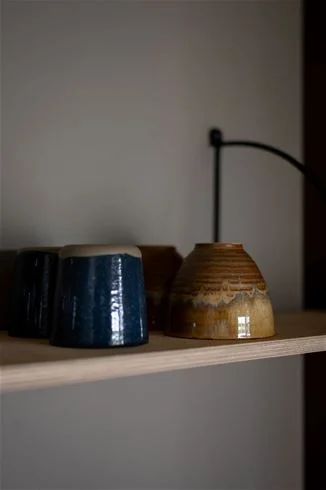 Alt-text: "Interiörbild från Skuleberget Havscamping med rustik belysning, keramik och hyllor fyllda med stengodskärl, vilket skapar en naturlig och inbjudande atmosfär."