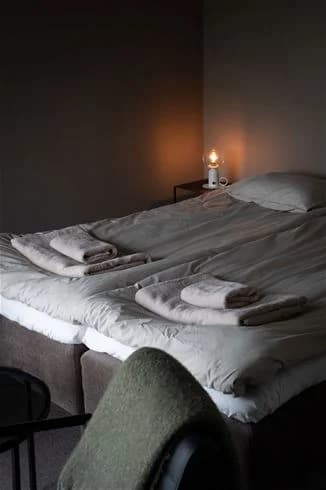 Ett ljust och inbjudande sovrum på Skuleberget Havscamping med en stor säng bäddad med vita lakan, trägolv och enkel inredning.