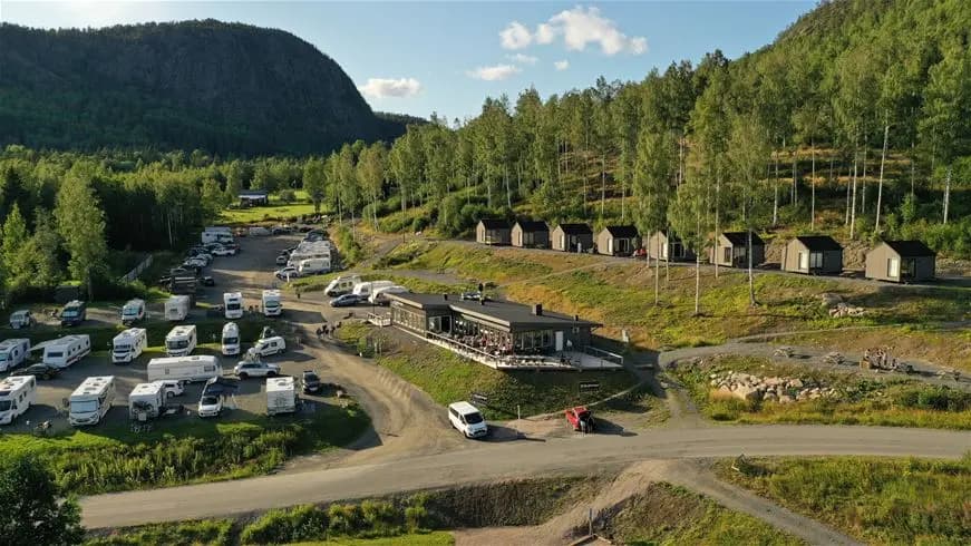 Flygbild över Skuleberget Havscamping med omgivande landskap. Berg och grönska omger campingen, och små hus syns i området. Bergspass och lantlig miljö ger en känsla av avskildhet och naturskönhet.