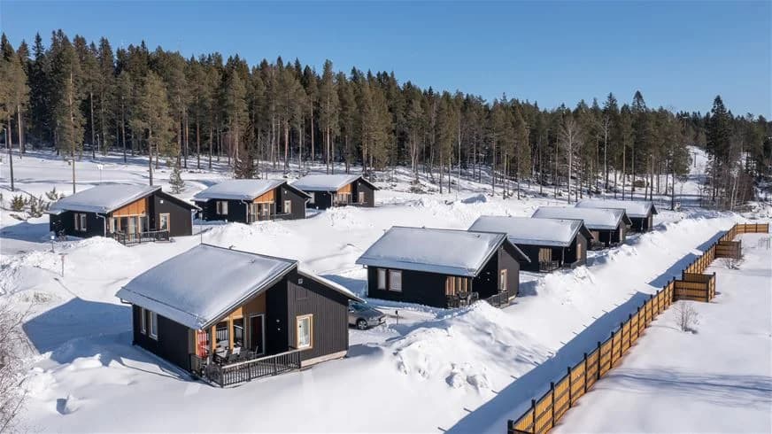 En snötäckt timmerstuga vid Skellefteå Camping under vintern, omgiven av snö och frostig natur.