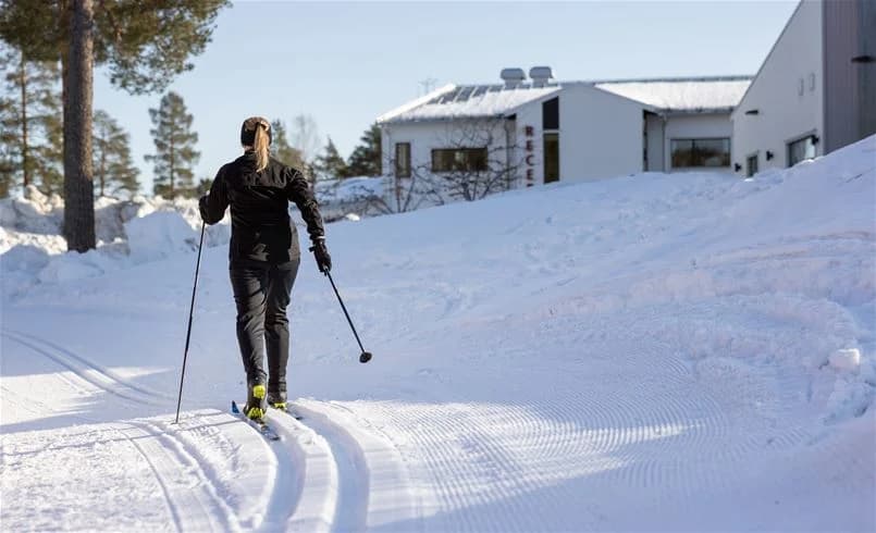 En vinterbild från Skellefteå Camping som visar snötäckta marker och en person klädd för skidåkning med utrustning som skidstavar och byxor, redo för vintersport.