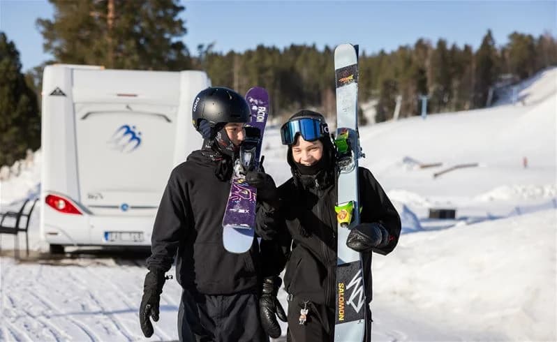 En person klädd i vinterkläder och hjälm, med skyddsglasögon och skidutrustning, står redo för vintersport på Skellefteå camping.