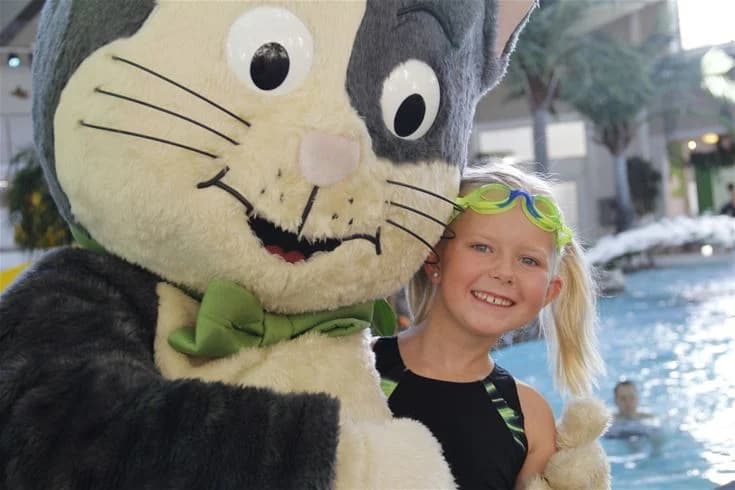 En leende maskot i form av en mjukdjur björn leker med ett glatt barn i en färgglad dräkt på Fyrishov stugby och camping, vilket ger en känsla av glädje och lekfullhet.