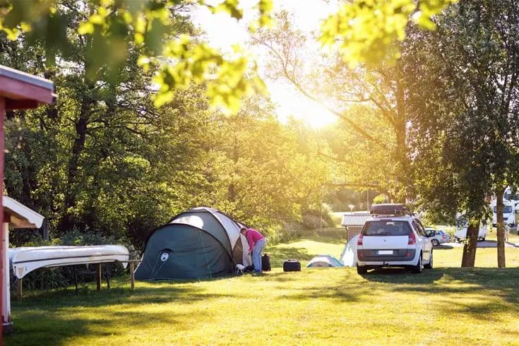 En campingplats vid Fyrishov med tält, husbilar och utomhusutrustning. Området omges av grönska, vilket skapar en naturnära och avkopplande atmosfär för besökare.
