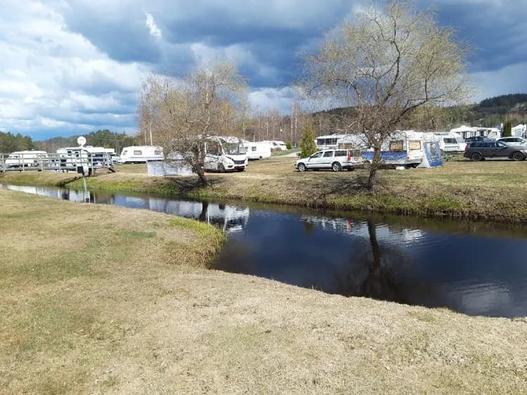 En husbil parkerad vid en flod med breda strandzoner och våtmarker, omgiven av grönska vid Bullarebygdens familjecamping.