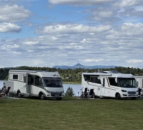 En bild på flera husvagnar uppställda på Särna Camping, omgivna av grönska och skog i en naturskön miljö.