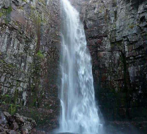 Ett kraftfullt vattenfall forsar ner över släta stenformationer omgivna av grönska vid Särna camping, ett populärt turistmål.