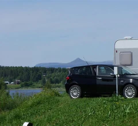 En bil med hatchback-design står parkerad på en campingplats omgiven av grönska vid Särna camping.