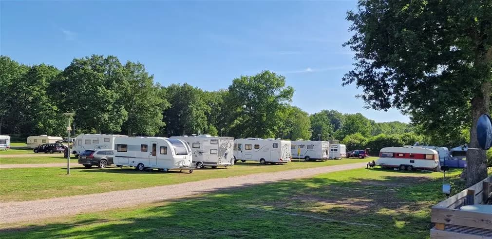 En husbil och en husvagn parkerade på en campingplats i ett naturnära område med träd i bakgrunden.