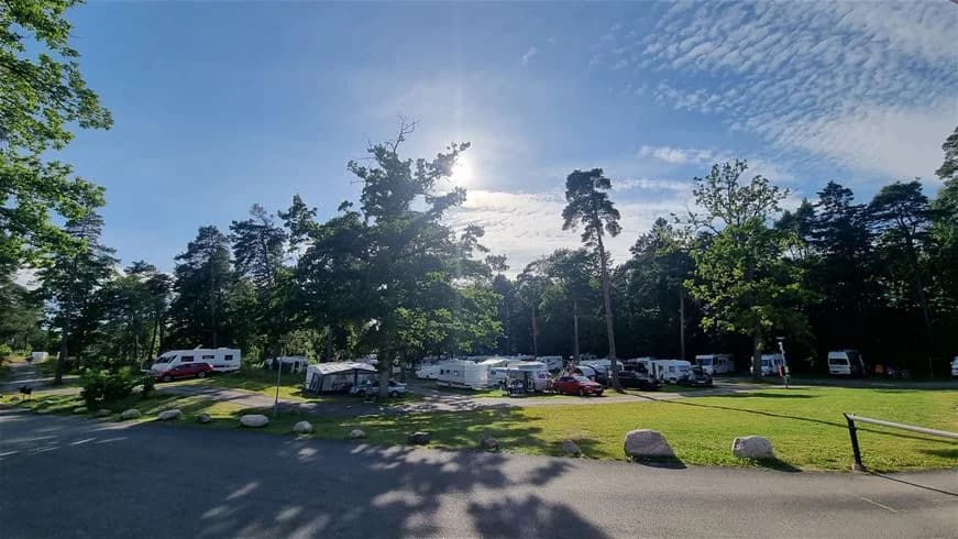 En campingplats i Trollhättan med husbilar parkerade på grusytor omgivna av gröna träd och gräsmattor.
