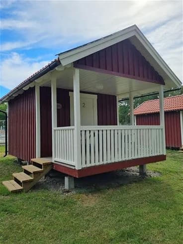 En trästuga med veranda vid Trollhättans Camping City, omgiven av grönska.