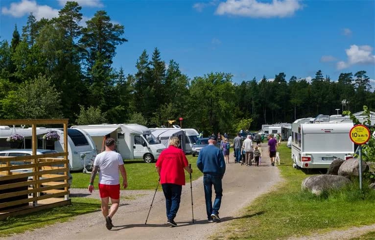 En trevlig campingplats i Trollhättan med träd i bakgrunden, campare som njuter av fritiden nära sina husvagnar och tält. En avkopplande plats för semester och rekreation.