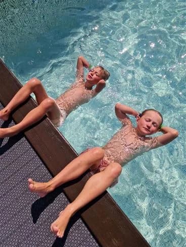 En grupp människor njuter av sommardagen runt en swimmingpool på Stenrösets camping i Trollhättan. Några är barfota och ser ut att ha roligt och koppla av i semestermiljön.