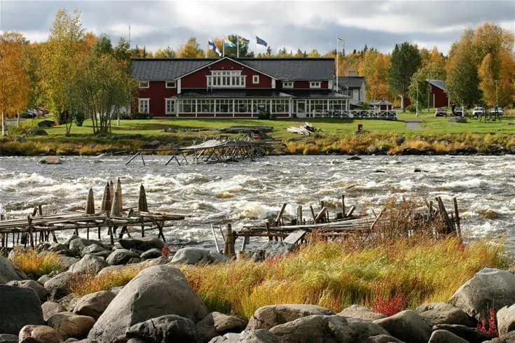 En vidsträckt flodlandskap med forsande vatten och omgivande gröna stränder vid Kukkolaforsen, perfekt för naturälskare och rekreation.
