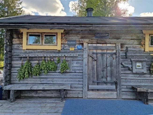 En rustik timmerstuga med träfasad och en välkomnande dörr, omgiven av grönska, vid Kukkolaforsen turist & konferens.