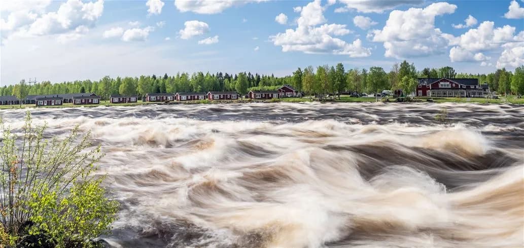 En forsande älv med strida strömmar omgiven av grönskande barrträd vid Kukkolaforsen turist & konferens.