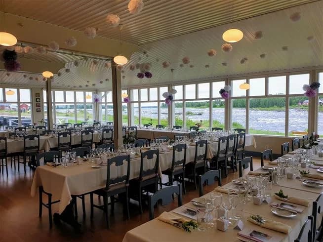 Bild av Kukkolaforsen Turist & Konferens: En charmig byggnad belägen vid en lugn fors, omgiven av grönska och våtmarksområde. Byggnaden fungerar som både restaurang och ekologiskt hotell och erbjuder en idyllisk naturupplevelse.