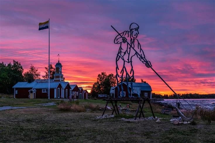 En dramatisk himmel vid Kukkolaforsen i skymningsläs, där silhuetter av träd och landskap avtecknar sig mot en färgglad himmel i varma toner av orange och rött.