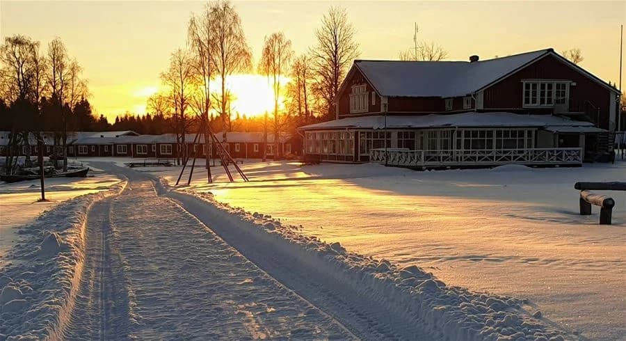 En snöigt vinterlandskap vid skymning med en charmig stuga omgiven av is och snö. Mörkret börjar falla och platsen ger en fridfull atmosfär vid Kukkolaforsen turist & konferens.