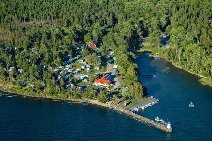 En sjö vid kusten med fritidsaktiviteter, flera båtar ligger förtöjda vid stranden nära skogsområde.