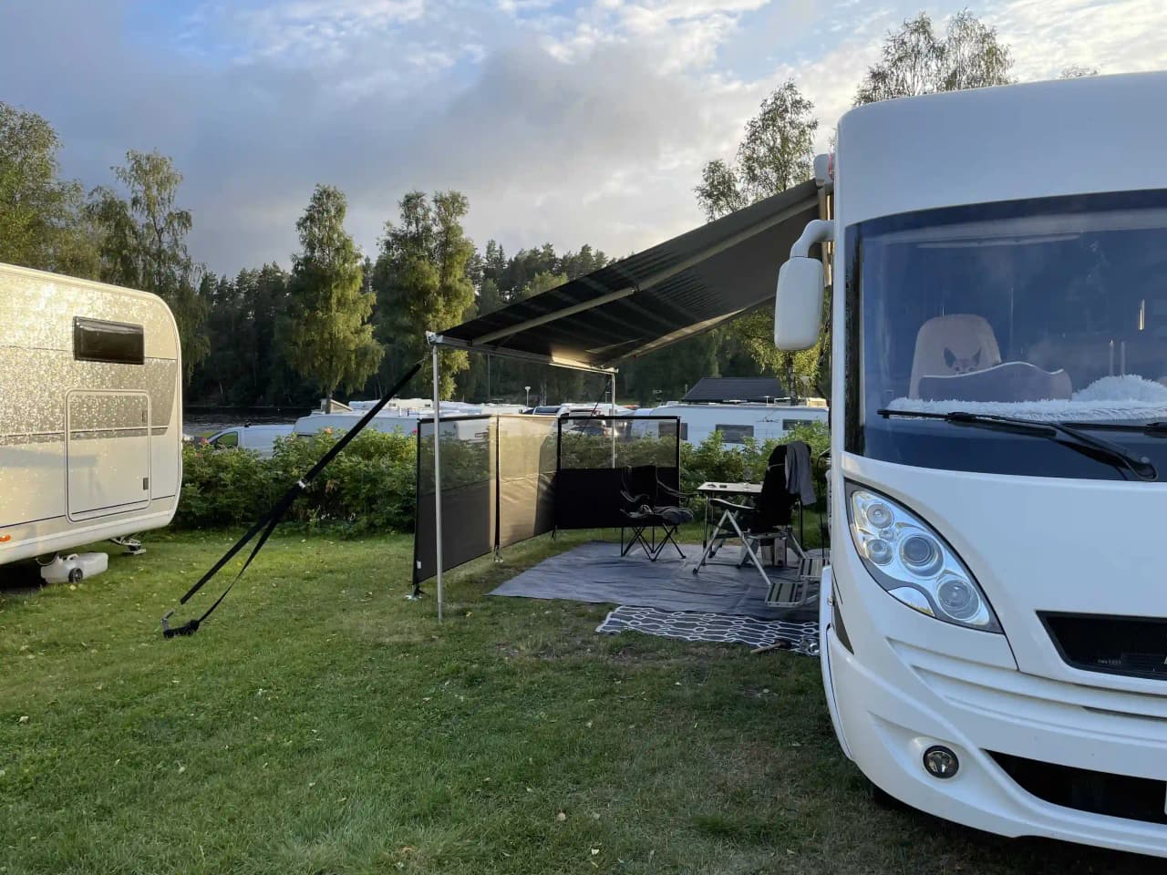 En husvagn och ett tält står uppställda på en grön campingplats vid Ragnerudssjöns camping och stugby, delvis skuggade av ett tak.