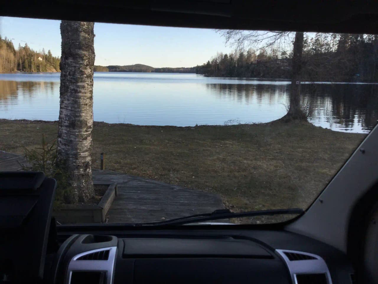 En bil med spegelreflektion av sjön Ragnerudssjön, omgiven av natursköna vyer, syns reflekterad i bilens sidospegel under en bilresa vid campingen.