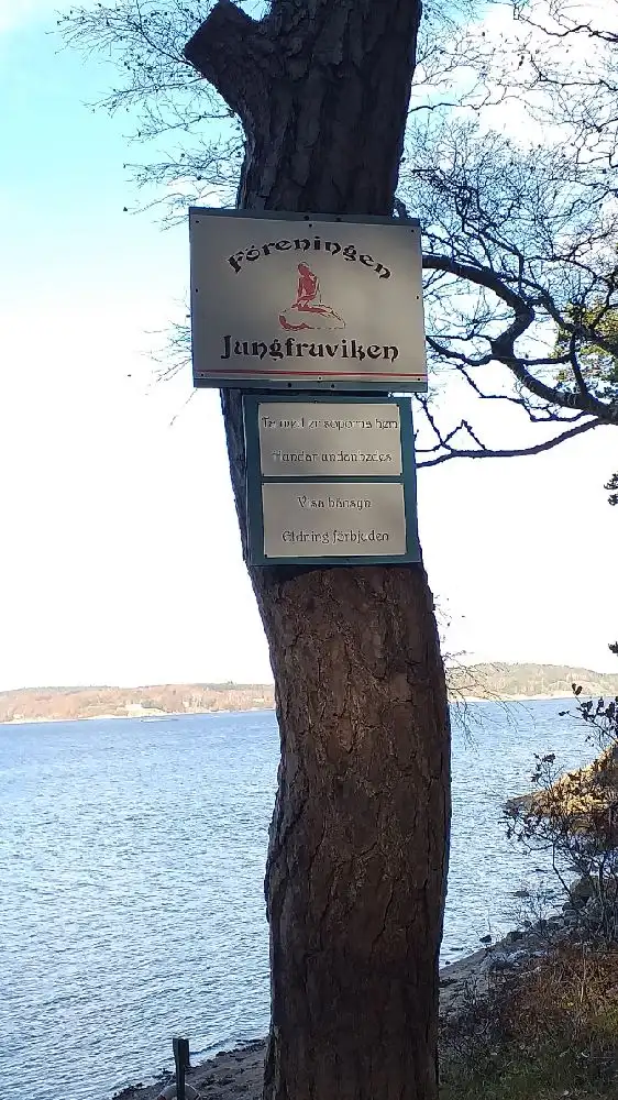 Solnedgång över kustlandskap vid Stenungsögården, med silhuetten av en skylt och havet i bakgrunden.