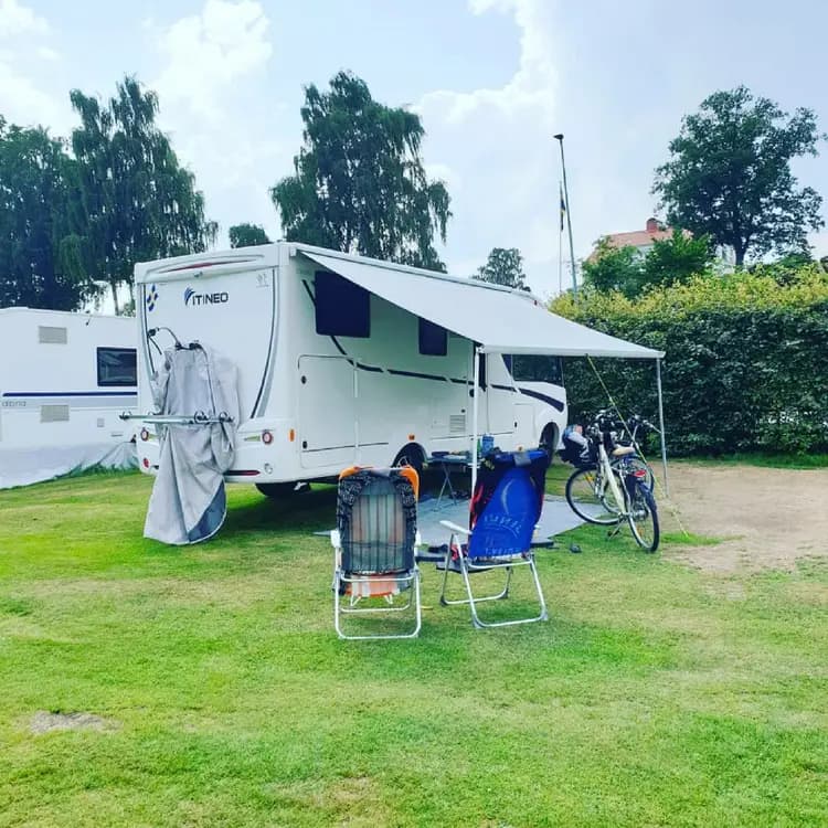 Bild på Öjaby camping som visar flertalet husbilar och husvagnar parkerade under skuggande träd. Det finns även tält och andra campingutrustningar uppställda runtom.