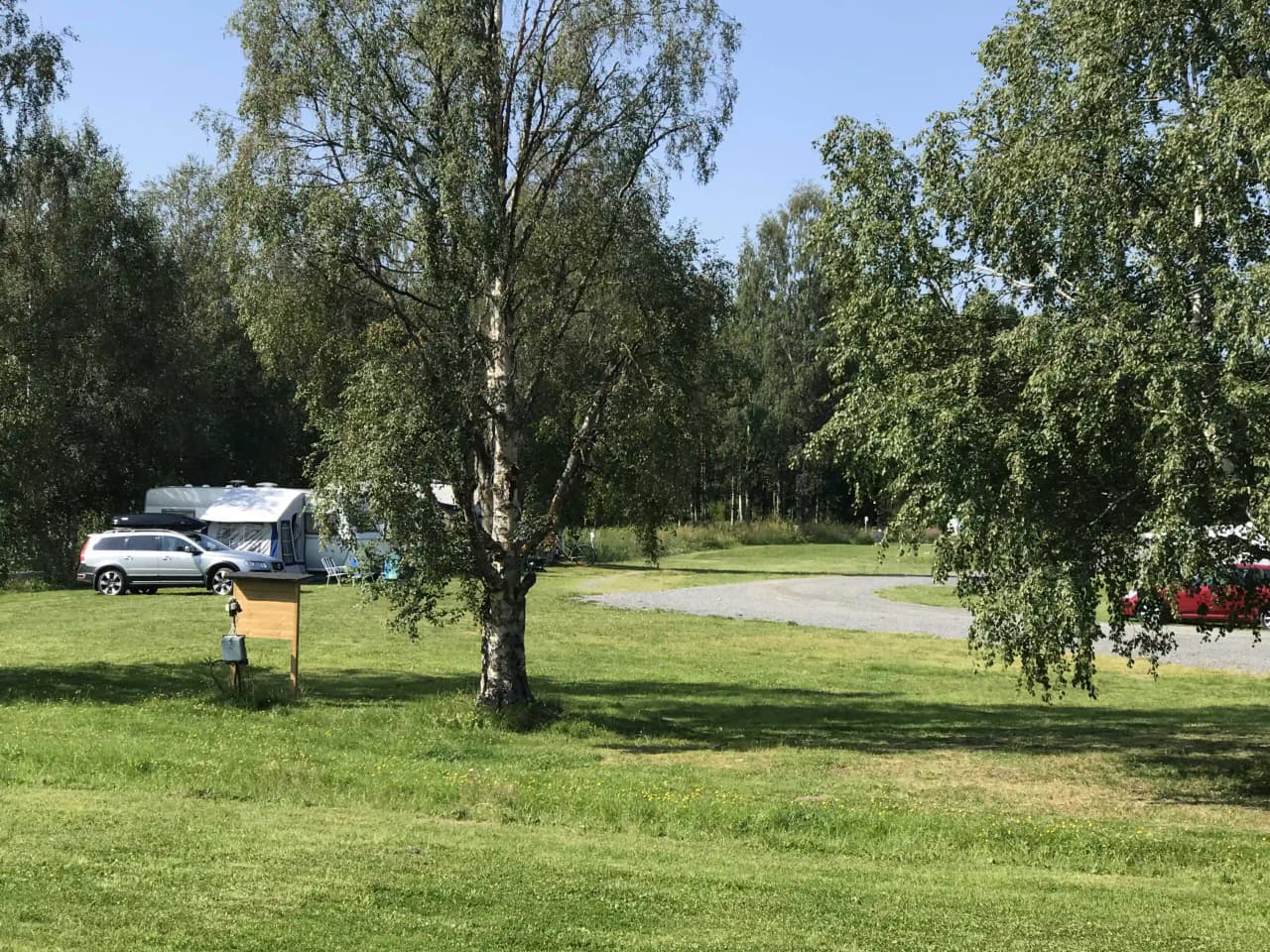 En grön campingplats omgiven av träd och gräs, med en husbil parkerad på en klippt gräsyta vid Ånge Camping.
