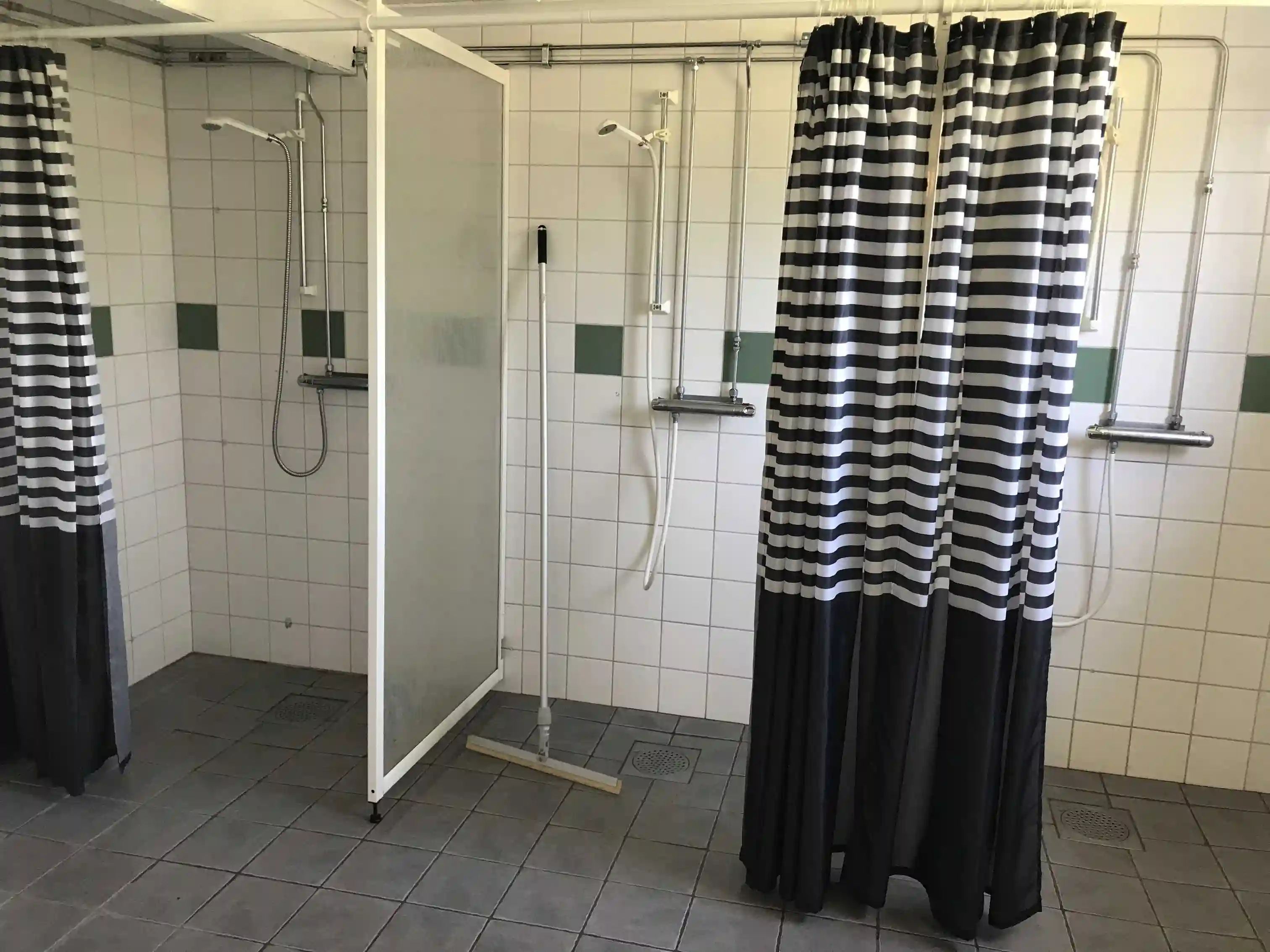 Alt-text: "Interiör av ett badrum på Ånge Camping med kaklade väggar, ett duschdraperi och golvplattor."
