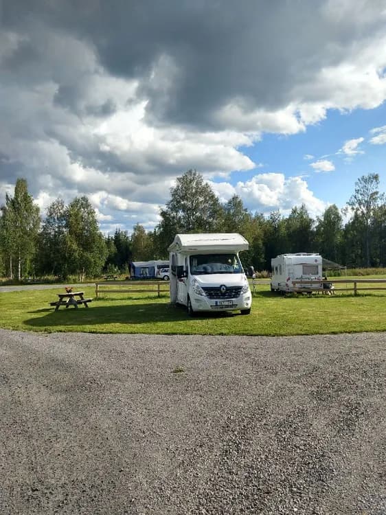 En campingplats med husvagnar och husbilar parkerade under en molnig himmel, omgivna av grönskande natur.