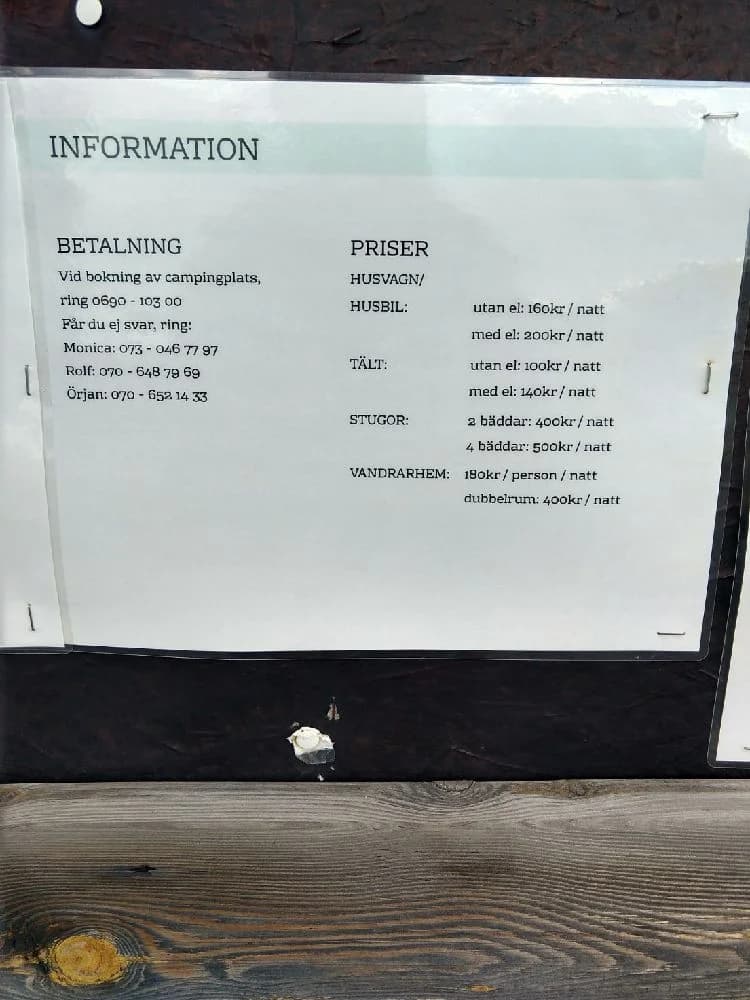 En idyllisk vy över Ånge Camping med tält och husvagnar på gröna ängar, omgiven av frodig skog och en klarblå himmel i bakgrunden.