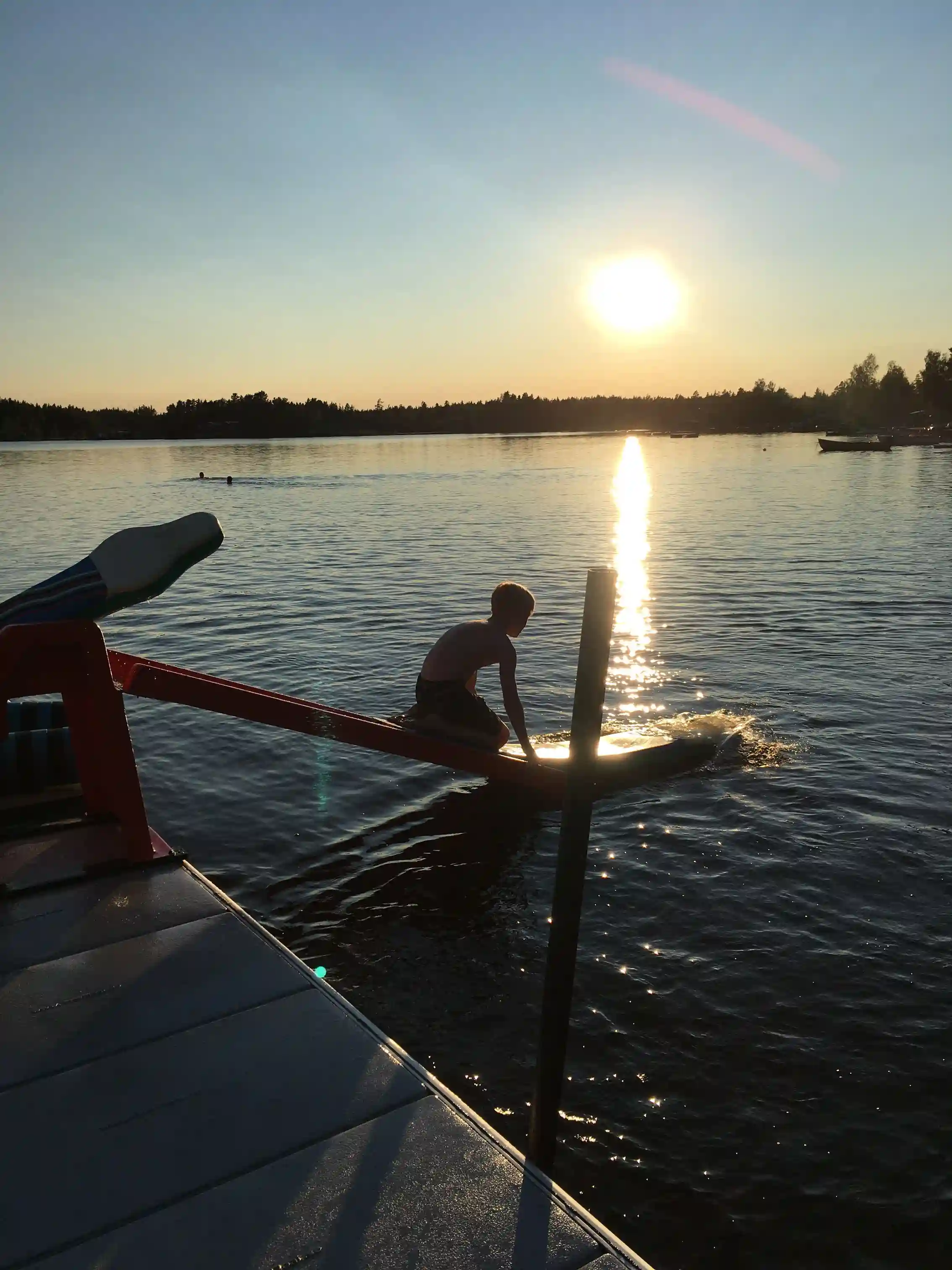 En sjö vid skymningen med båtar förtöjda vid en brygga, omgiven av stilla vatten och en vacker solnedgångshimmel.
