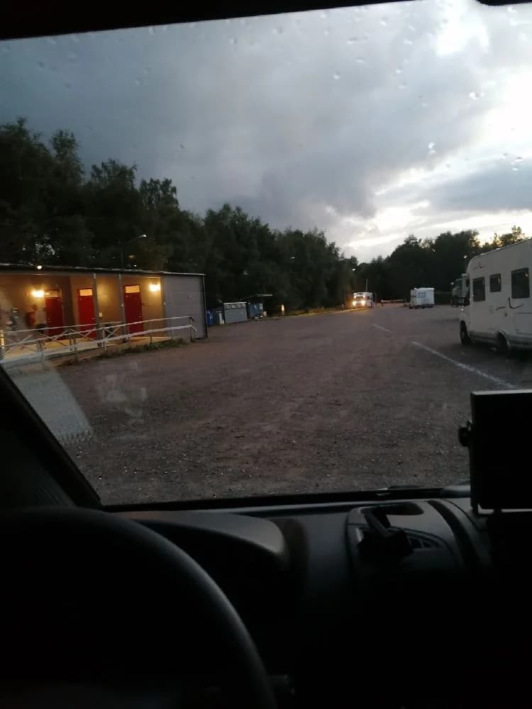 En sportbil står parkerad på asfalt med träd och fält i bakgrunden, vilket ger en känsla av en startpunkt för en sommarutflykt.