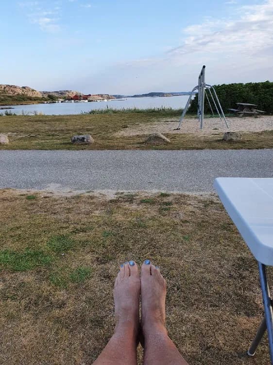 En somrig scen på Saltviks camping med utomhusmöbler där människor njuter av fritid, avkoppling och semester. Några personer är barfota på stranden, vilket förstärker sommarkänslan.
