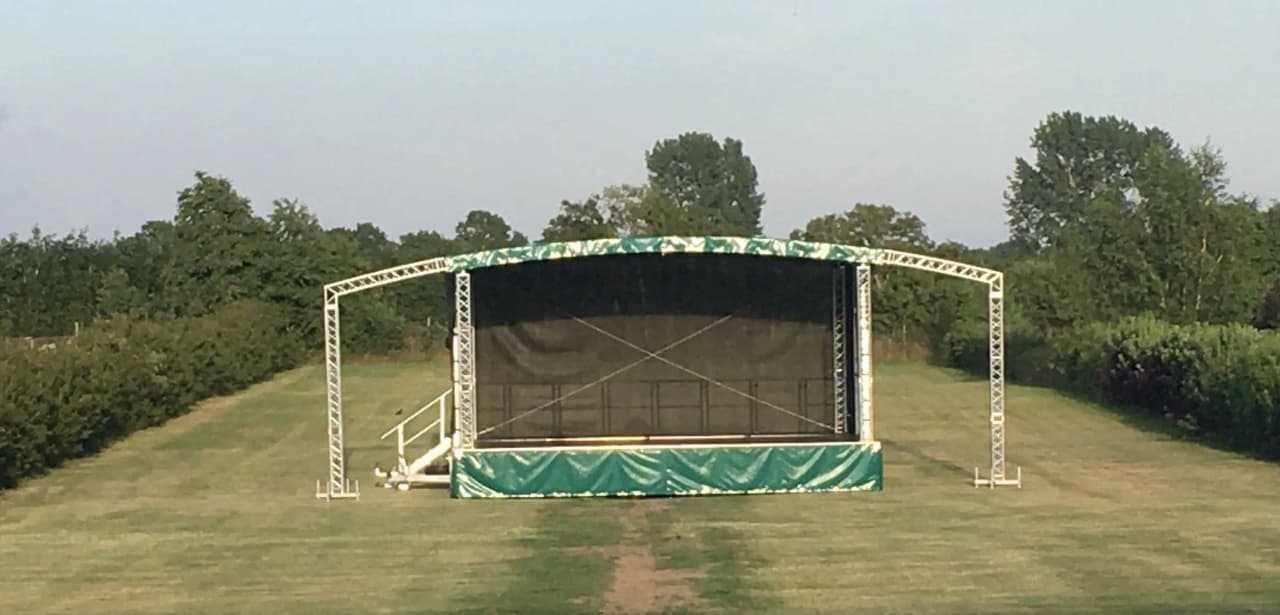 Bild av Bläsinge Gård: En grönskande gårdsmiljö med en välskött gräsmatta och ett skuggande paviljongtak i mitten. Strukturen verkar vara en utomhusscen med konstgjort gräs runt omkring.