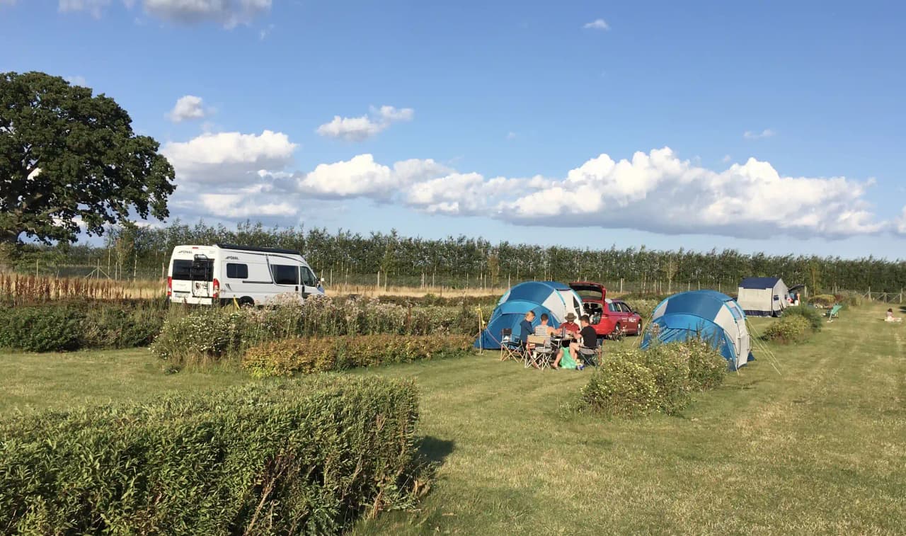 En campingplats på Bläsinge gård med tält och husbilar omgivna av öppna fält och vidsträckt landskap.