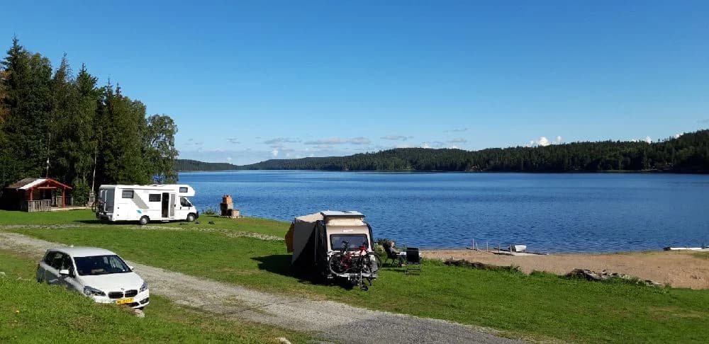 En rofylld vy över en sjö med båtar vid kusten, omgiven av gröna backar, vid Gröna Backe Camping & Stugor.