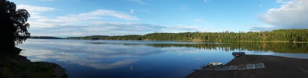 En naturskön vy vid Gröna Backe Camping & Stugor med en stilla blåvattenyta omgiven av grönska och naturmiljö.