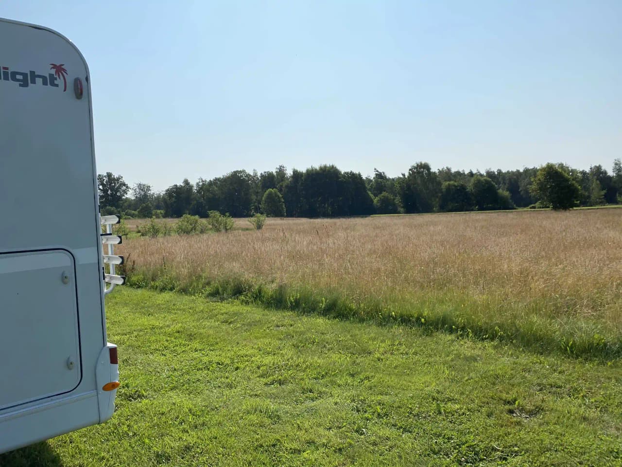 En grön och vidsträckt äng med husbilar parkerade på Vinslövs camping under en klarblå himmel.