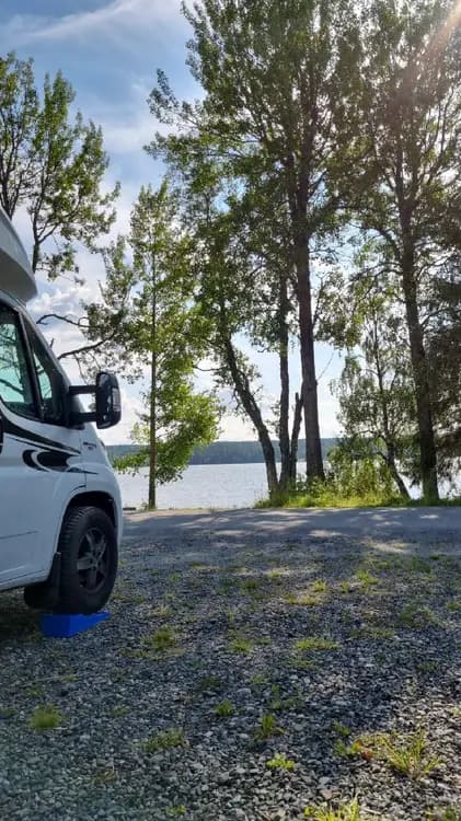 En parkerad husbil med öppna dörrar vid Trångsvikens bygdegård, omgiven av grönska och landsbygdsmiljö.