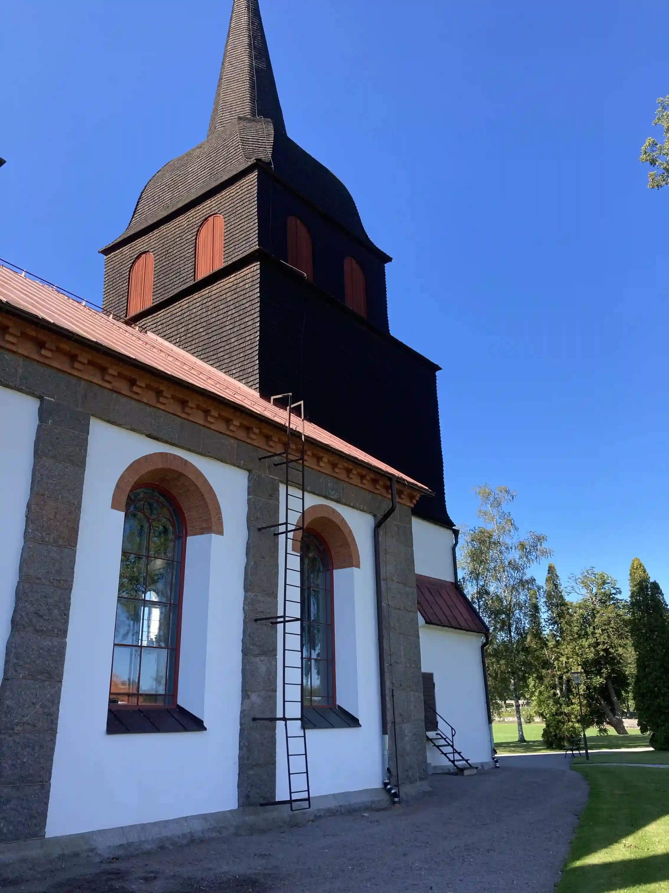 En pittoresk kyrka med ett brant, spetsigt kyrktorn omgiven av frodig grönska, typisk för landsbygden nära Vimmerby Camping - Nossenbaden.